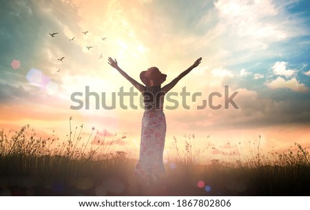 Praise and worship God concept: Silhouette of healthy woman raised hands at meadow sunset background
