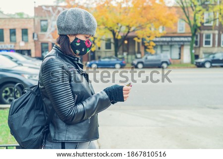 A profile of a young woman with a face mask looking at a cell phone in a street