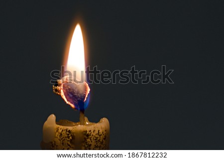 bright yellow flame of a candle close up burns its own wick on dark background