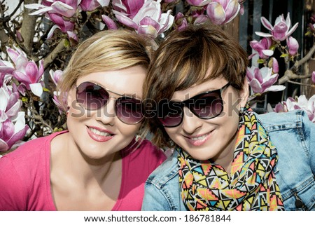 Two young caucasian women posing with blooming magnolia. Women's beauty and fashion.