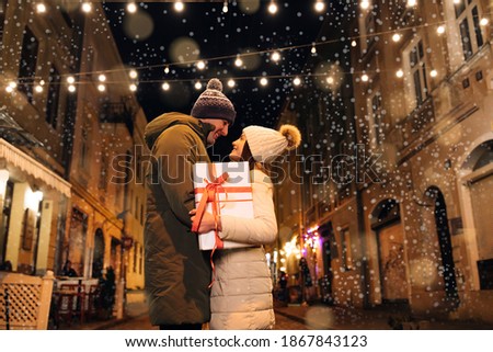 Christmas gifts exchange. Xmas celebration together. Smiling couple celebrating Xmas eve together at bright garland decoration