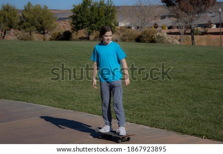 A little girl in a blue t-shirt and sweat pants skating down the sidewalk of a park in the fall season.
