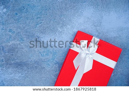 Red gift with white bow on blue concrete background. Merry Christmas, New Year, Birthday, Valentine, card concept. Top view, flat lay, copy space