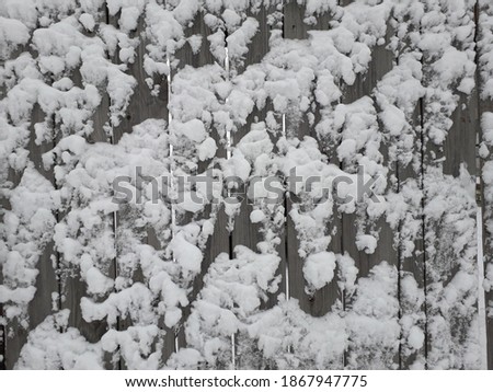 A wooden wall with snow sticking to it. Fence made of old gray boards. Winter background.