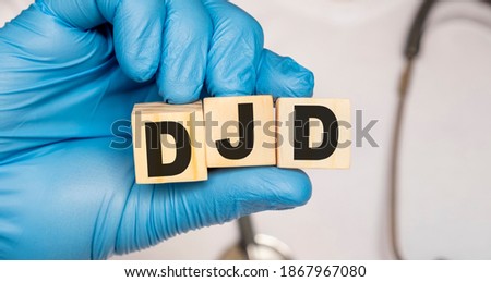 DJD Degenerative joint disease - word from wooden blocks with letters holding by a doctor's hands in medical protective gloves. Medical concept.