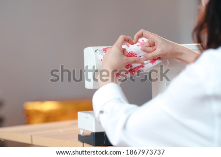 A girl making a heart sign with her fingers, sewing machine on the background. Hobby and part-time job concept.