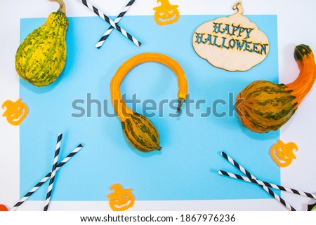 Whimsically curved pumpkin on a blue background, Halloween concept, blue paper background, wooden sign with the text "Happy Halloween", cocktail straws.
