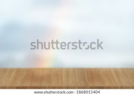 Empty warm wooden table with green park nature outdoor background blue sky and rainbow is graphic resource template mock up for display of product