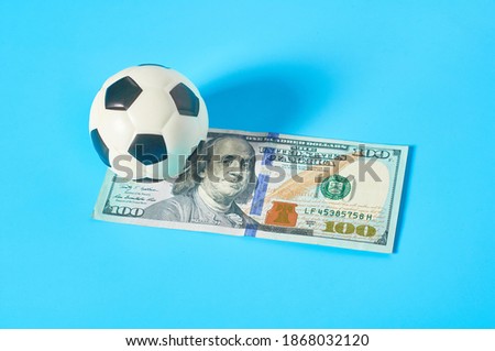Soccer, football ball and banknote of 100 dollars on blue background. Purchasing sport accessories. Concept of corruption in sport