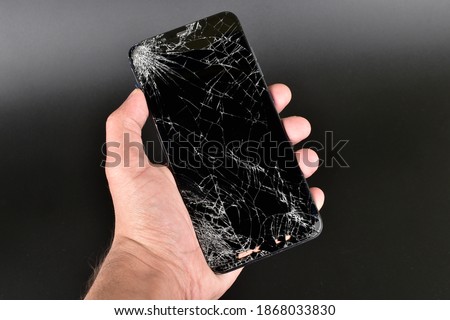 broken screen smartphone in hand on black background, shattered screen