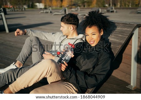 an African-American woman and a Latin man sit in comfortable outdoor sports clothing. a sporty couple drink water during a morning jog in the city's Central Park. Autumn sports fitness.