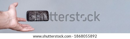 Hand holding mobile phone with broken screen on grey background. banner with copy space