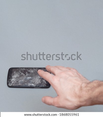 Hand trying to catch a falling phone. mobile phone with broken screen on grey background
