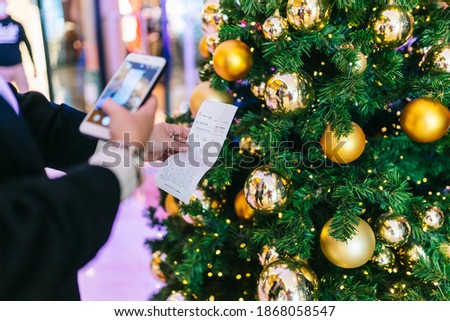 An unrecognizable person takes a photo of a ticket with his telephone with a Christmas tree in the background