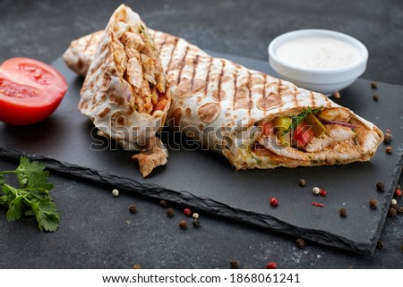 Shawarma with meat, cutaway, with sauce, tomatoes, cheese, herbs and garlic, on black slate, on a black background Royalty-Free Stock Photo #1868061241