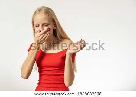 Teenage girl with blond hair and in a red dress sneezes