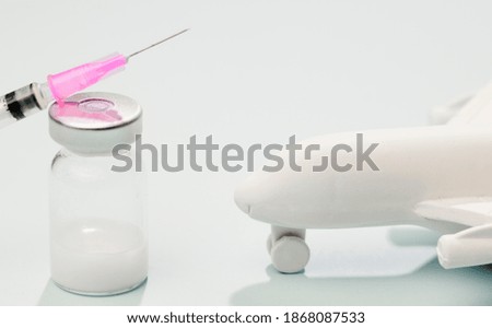 Vaccine in glass vial, with syringe, white plane, blue background.