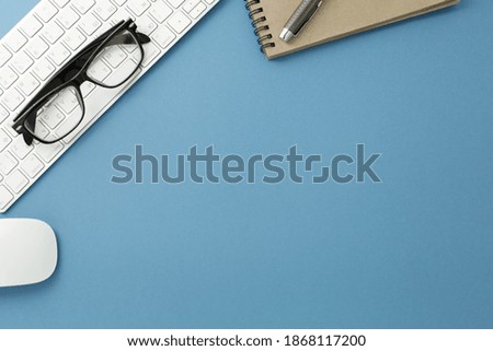 Glasses keyboard notepad mouse and pen on blue background