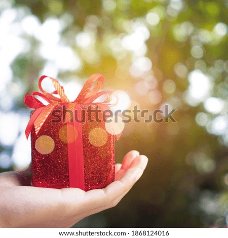 Hand hold gift box to someone on green bokeh nature. Celebration holiday concept.