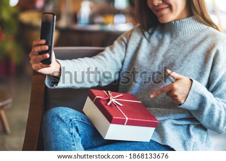 Closeup image of a beautiful young asian woman using mobile phone to take selfie with gift box