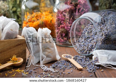 Filter tea bags filled with medicinal herbs. Glass jar of dry lavender flowers for making herbal tea, jars of various healthy herbs on background. Alternative medicine.
