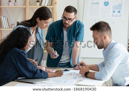 Motivated multiracial diverse businesspeople brainstorm work together on paperwork at team meeting in office. Concentrated young multiethnic colleagues discuss business ideas. Teamwork concept. Royalty-Free Stock Photo #1868190430