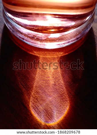 
The shadow from the light reflection of a glass of black tea, by the sunrise, in the morning. Forms an abstrack shape. beautiful and amazing picture. Clear and brown,  on the wooden table. Silhouette