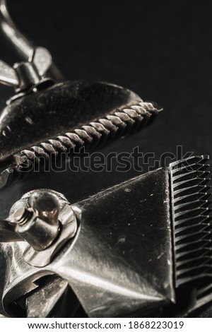 On a black surface are old barber tools.Two vintage manual hair clipper. black monochrome. Close-up. Barbershop background. contrast shadows. vertical