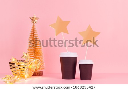 Christmas coffee mock up - gold christmas tree, lights, blank tage with black paper cups on pink background, template for advertising, design, cafe, restaurant, bar.