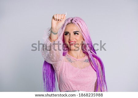 Portrait of a young modern girl with pink braids hair showing fist looking away with a smile. White background.