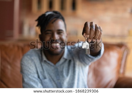 Close up focus on keys in smiling african american guy hands. Happy young mixed race biracial man feeling excited of purchasing own apartment, moving into new house, real estate rental service concept Royalty-Free Stock Photo #1868239306