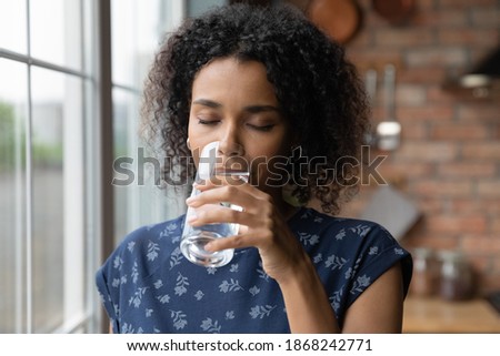 Head shot young african ethnicity woman drinking mineral water, refreshing organism in kitchen. Thirsty millennial multiracial lady feeling energetic in morning at home, hood healthcare daily habit. Royalty-Free Stock Photo #1868242771