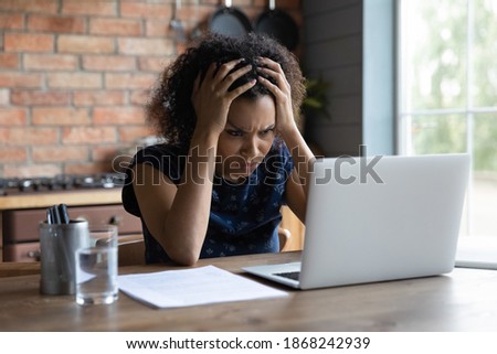 Confused young african ethnicity woman looking at computer screen, feeling stressed of reading bad news, getting dismissal notice by email, bank loan rejection notification, unlucky people concept. Royalty-Free Stock Photo #1868242939