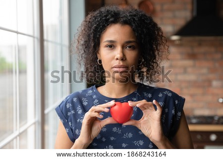 Thoughtful young african ethnicity female volunteer holding heart in hands. showing support to vulnerable people. Kind millennial biracial woman feeling thankful, gratitude or empathy concept. Royalty-Free Stock Photo #1868243164