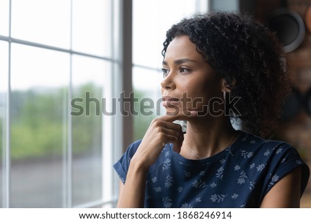 Thoughtful millennial african american woman standing near window, recollecting memories or feeling lonely at home. Pensive young biracial lady contemplating, lost in thoughts, vision concept. Royalty-Free Stock Photo #1868246914