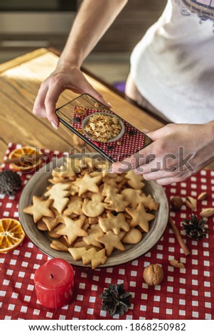 A woman is taking photos a plate with delicious homemade figure holiday cookies on her phone camera.
