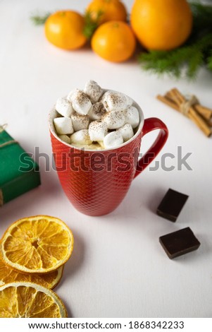 Red mug with hot drink and marshmallows. Green gift box, Christmas tree, orange and tangerines. White background