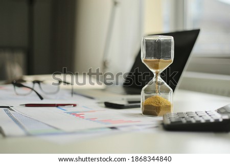 Hourglass and computer standing on graph or analytical papers, business  equipment. 