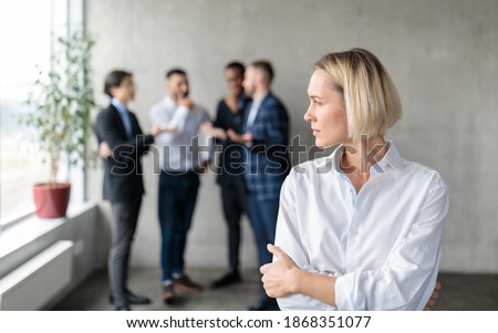 Male Coworkers Whispering Behind Back Of Unhappy Businesswoman Spreading Rumors And Gossips Standing In Modern Office. Sexism And Bullying Problem At Workplace Concept. Selective Focus Royalty-Free Stock Photo #1868351077