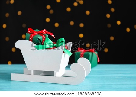Sleigh with gift boxes on turquoise wooden table against blurred lights