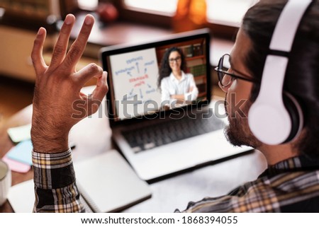 E-Learning And Remote Study. Student Guy Gesturing Okay To Distant Teacher Having Online Class Sitting At Laptop At Home. Modern Education, Distance Learning Concept. Back View, Selective Focus
