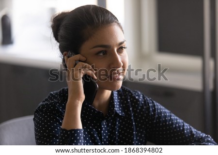 Enjoying phone talk with pleasant person. Smiling young indian lady making call engaged in conversation holding phone close to ear. Peaceful millennial hindu female speak on cell listen to good news Royalty-Free Stock Photo #1868394802