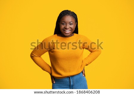 Cheerful Lady. Portrait Of Happy Smiling African American Female Over Yellow Background, Positive Black Millennial Woman In Stylish Sweater Posing With Hands On Hips And Looking At Camera, Copy Space