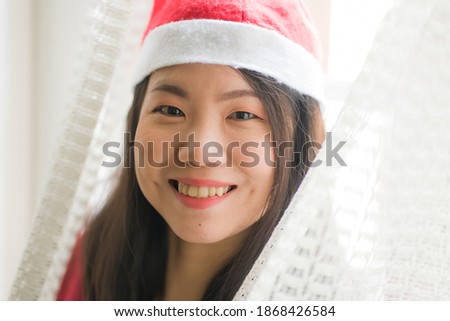 lifestyle home portrait of young beautiful and happy Asian Chinese woman in Santa Claus hat and red jersey enjoying Christmas time smiling cheerful 