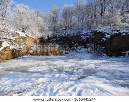 Rocks in the snow. Snow-covered trees at the top of the rocks. Frozen pond under the rocks. Beautiful landscape in sunny winter weather.