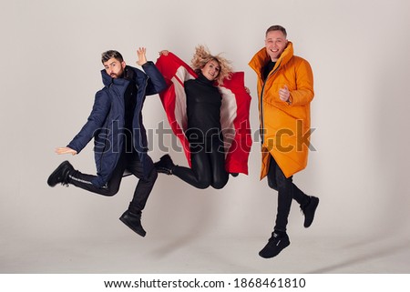 Eject of blur from jump dynamics. Three models on a white background are dressed in winter clothes of different colors. The emotion of joy and delight. Three friends fooling around