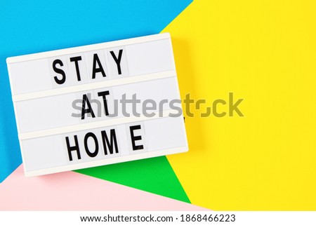 Lightbox with text STAY AT HOME on yellow, green, pink and light blue background. Top view