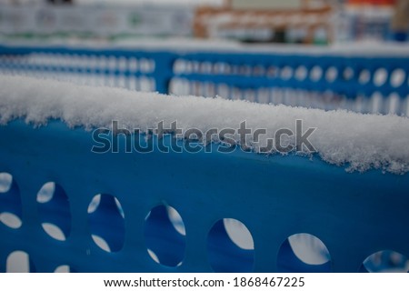 Blue plastic fence with holes in winter. Visible snow resting on the upper horizontal part of the fence.