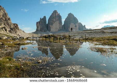 A man enjoying the view on the famous Tre Cime di Lavaredo (Drei Zinnen), mountains in Italian Dolomites. The mountains are reflecting in small paddle. Desolated and raw landscape. Natural phenomenon