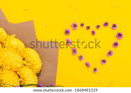 Small pink chrysanthemums in the shape of a heart and a large bouquet of lush flowers on bright yellow background with copy space. Holiday card for the holiday of all lovers. Happy Valentine's Day.